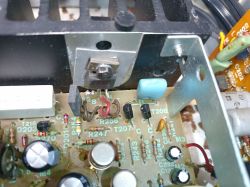 Zbliżenie na wnętrze urządzenia elektronicznego, pokazujące płytkę drukowaną ze ścieżkami, elementami elektronicznymi i przewodami.