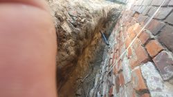 Odsłonięty fundament ceglanej ściany budynku i wykop na głębokość około 1,5 metra