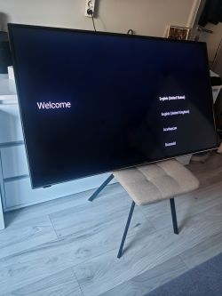 Telewizor na krześle z ekranem „Welcome” i listą języków po prawej stronie.