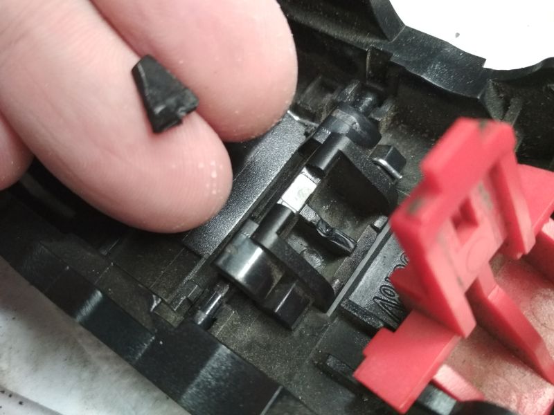 Zbliżenie na wnętrze obudowy akumulatora, dłoń trzyma oderwany kawałek czarnego plastiku, widoczny również element czerwony.