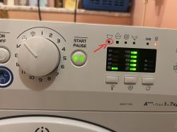 Panel pralki Indesit z podświetlonymi diodami; czerwona strzałka wskazuje migającą kontrolkę cyklu