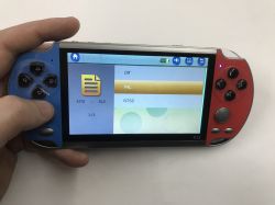 Handheld X12 console in a hand, screen showing TV-out settings menu: Off, PAL, NTSC