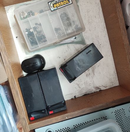 Pudełko z elementami elektronicznymi i trzy baterie na drewnianym blacie.