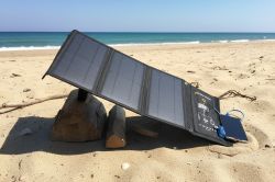 Foldable solar panel on a beach, propped up on wood blocks and charging a smartphone