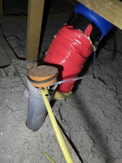 Rura wentylacyjna na poddaszu z trójnikiem i taśmą izolacyjną w pobliżu.