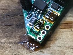 Close-up of a green PCB corner with SMD parts on a wooden surface and a small liquid spill