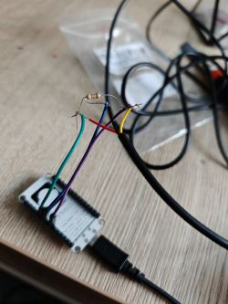 NodeMCU v2 Connection with DS18B20 Sensor and Resistor NodeMCU v2 board with connected wires and a resistor, lying on a wooden table.