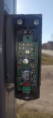 Zbliżenie na fotokomórkę do bramy automatycznej z widoczną płytką drukowaną i elementami elektronicznymi.