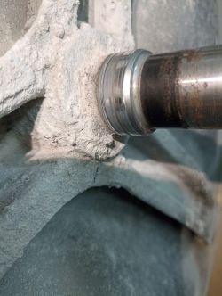 Zdjęcie zbliżeniowe metalowego wału obudowanego betonową lub kamienną strukturą z widocznymi śladami korozji.