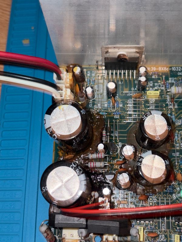 Zbliżenie na uszkodzoną płytkę PCB z kondensatorami i zalanym klejem