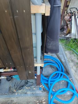 PVC pipe installed on a wooden structure with blue hoses on the ground.