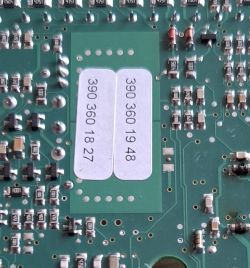 Zbliżenie na fragment płytki PCB modułu elektronicznego z widocznymi rezystorami oraz dwoma naklejonymi etykietami z numerami.