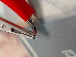 Czerwona żabka podłączona do diody umieszczonej na metalowym tle.