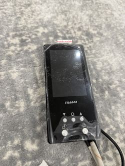 Black electronic module by Tilanco lying on a grey surface. The device features a display and several buttons.