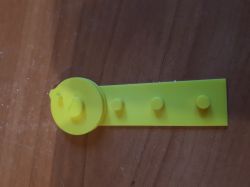 Żółta, plastikowa część z okrągłym elementem na tle drewnianej powierzchni.