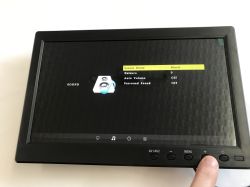 10-inch monitor showing the sound settings menu; a finger presses the “+” button on the bottom panel