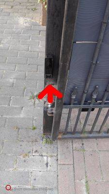 Brama przesuwna z czarnym profilem i zaznaczeniem czerwoną strzałką miejsca montażu fotokomórki.