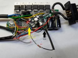 Zbliżenie na płytkę elektroniczną z kolorowymi kablami, kondensatorami i podpisanymi strzałkami.