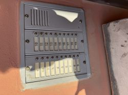 Panel domofonu z przyciskami i numerami mieszkań na tle różowej ściany