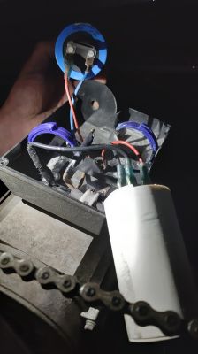 Obrazek przedstawia elementy elektryczne w skrzynce z przewodami, kondensator i łańcuch.