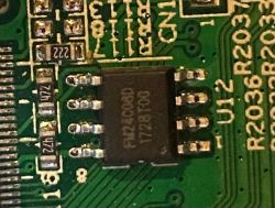 Zbliżenie na chip elektroniczny na zielonej płytce drukowanej, oznaczony jako FM25Q08D.