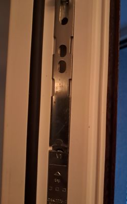 Zbliżenie na metalowy mechanizm w ramie drzwiowej z widoczną listwą zaczepową.