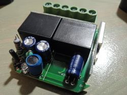 Photo of an electronic module with capacitors and relays on a green circuit board.