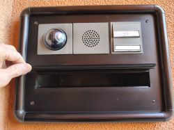 Mailbox with intercom panel; a hand lifts the mail slot flap