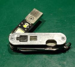 Scyzoryk z aluminiową okładziną i wysuniętym modułem USB z widoczną diodą LED na zielonym tle
