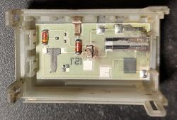 Wnętrze płytki elektronicznej z zaznaczonymi ścieżkami i elementami lutowanymi, znajdującej się w szarej obudowie.