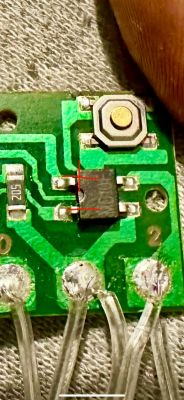 Zbliżenie na płytkę drukowaną z elementami elektronicznymi, z zaznaczonymi czerwonymi liniami punktami do zmostkowania.
