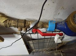Zawór z czerwoną rączką z plombą na metalowym drucie.