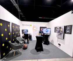 ELDAG trade show booth with screens, cocktail tables, chairs, and device panels on the walls