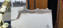Papier ceramiczny z ciemnymi przypaleniami trzymany obok dyszy palnika