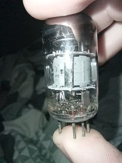 Zbliżenie lampy elektronowej trzymanej w palcach, widoczne styki i wnętrze.