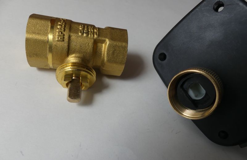 Brass valve with a square stem and threads next to a black housing with a brass threaded ring