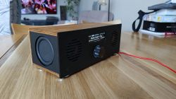 Wooden radio with black front and small display on a wooden table, with a red cable