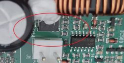 Zbliżenie na płytkę PCB z dużym kondensatorem, układem scalonym i czerwonym owalem zaznaczającym obszar.