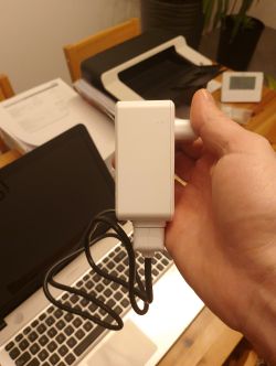 Osoba trzyma biały moduł elektryczny z przewodem nad laptopem na stole