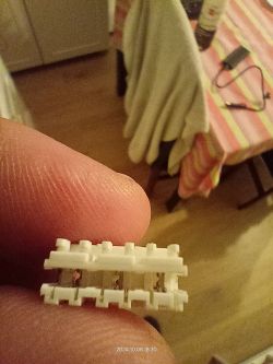 Biały złącze 3-pinowe trzymane w palcach na tle stołu.