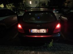 Tył czarnego hatchbacka Nissan nocą na parkingu, świecące tylne lampy i widoczna tablica rejestracyjna