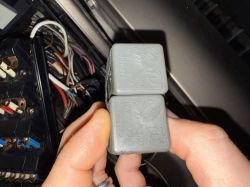 Ręce trzymające dwa przekaźniki samochodowe przed skrzynką bezpieczników.