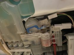 Zdjęcie wnętrza zmywarki Siemens SE64M36, ukazujące część mechanizmu z niebieską zapadką dźwigni.