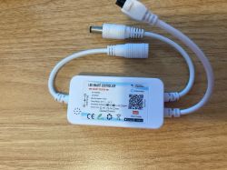 LED Smart Series Controller on a Desk White LED controller with two cables and technical label lying on a wooden surface.