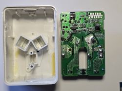 Disassembled device: white plastic housing and green PCB with electronic components on a tabletop