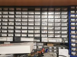 Ściana z organizerami na drobne elementy elektroniczne, szufladki opisane ręcznie markerem.