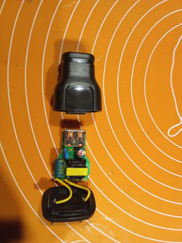 Rozłożona ładowarka USB z widoczną wewnętrzną elektroniką na pomarańczowym tle