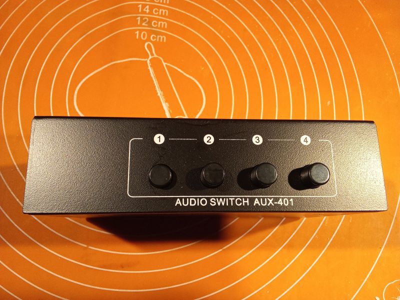 Przełącznik audio AUX-401 z czterema przyciskami na pomarańczowym tle.