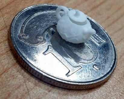 Mały wydruk 3D w ceramice przedstawiający czajniczek, umieszczony na monecie.