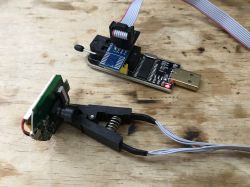 USB programmer with a clip for chip programming connected to a small PCB.